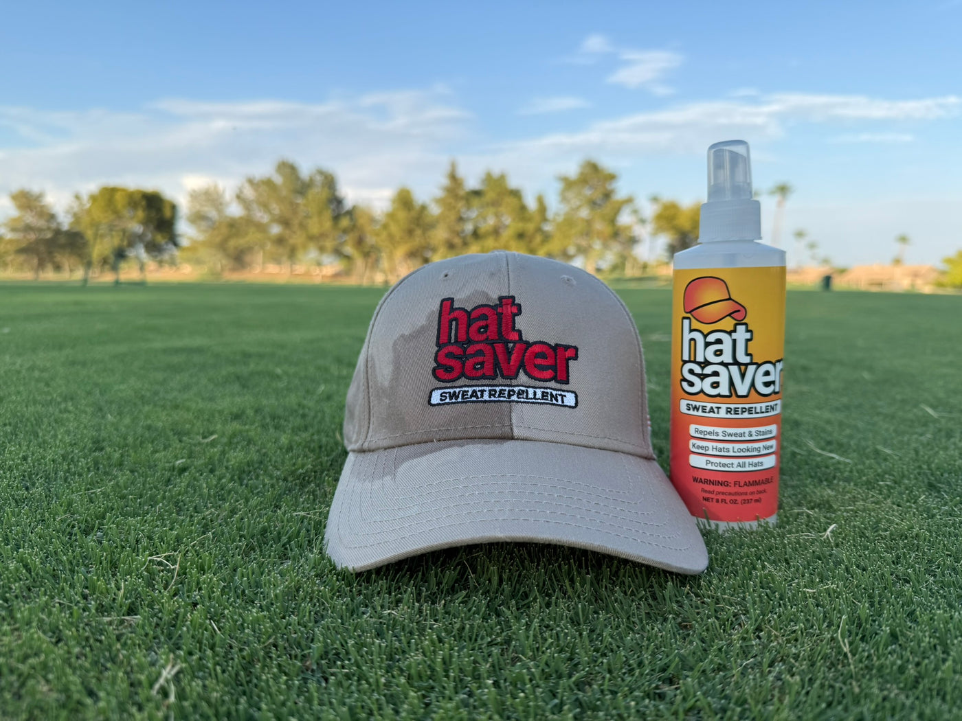 Hat stained cap and Hat Saver spray bottle on grass with trees in the background